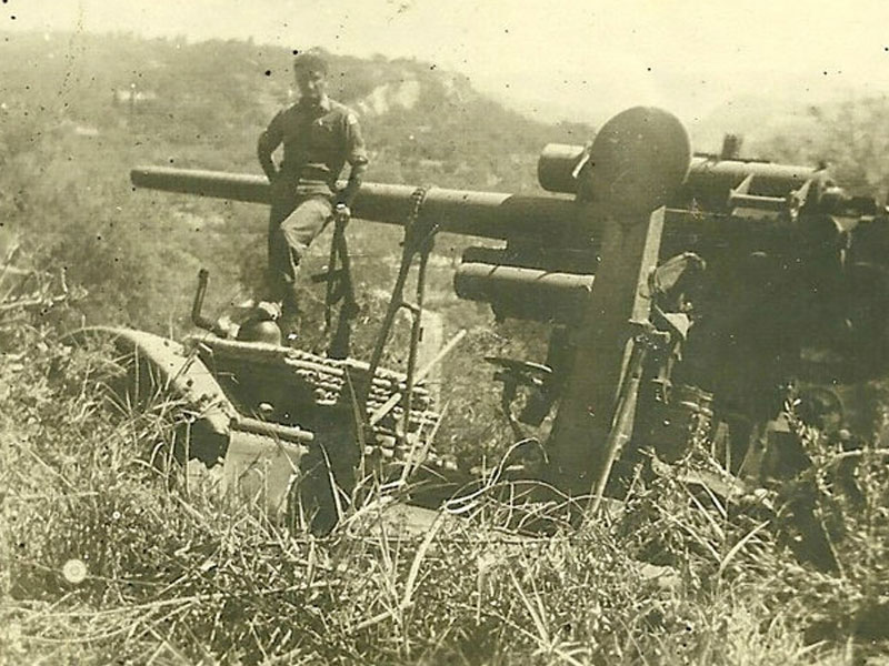 A black and white photograph of man standing with heavy artillery.